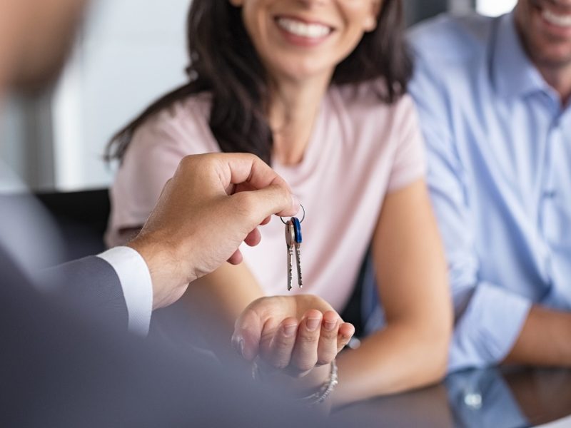 Close up of man hand giving house keys to woman. Smiling mature woman receiving new house keys from real estate agent. Man delivering keys to client for new home. Real estate agent giving keys to apartment owner.
